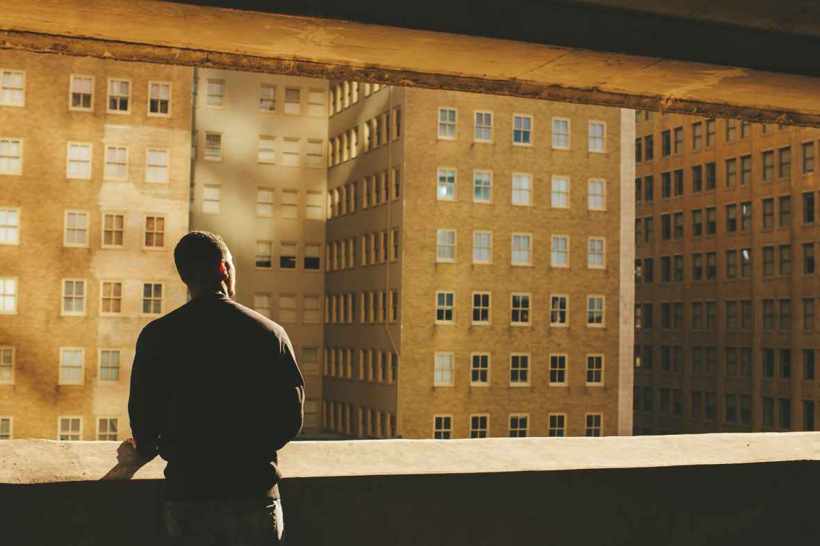man standing on rooftop facing brown highrise building